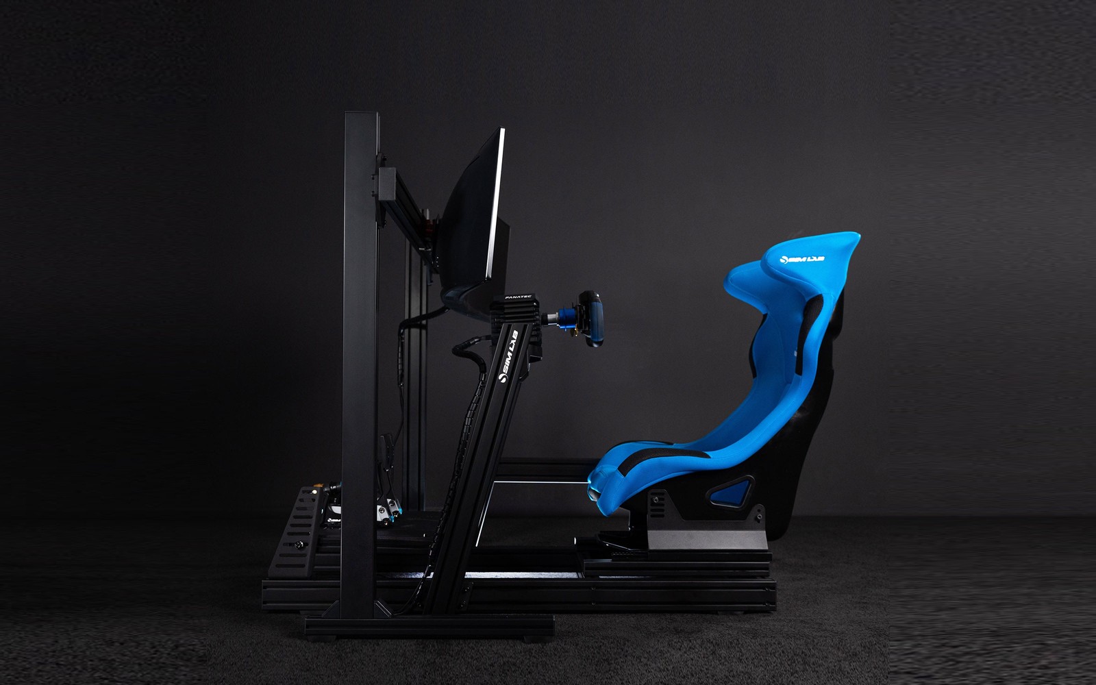 Cockpit Sim-Lab GT1 Pro visto de perfil, com um assento azul, um volante e uma tela grande, contra um fundo escuro